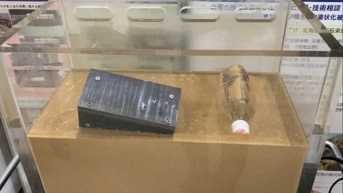 地盤が液状化して家の模型が倒れ、ペットボトルが浮上した模型(写真:日経クロステック)